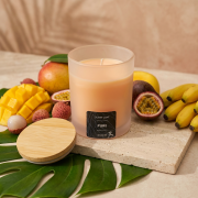 Orange Duftkerze im Glas („Pure“) mit Bambusdeckel in fruchtiger, tropischer Inszenierung mit Mango, Banane und Passionsfrucht
