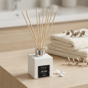 Raumduft-Diffusor mit Rattanstäben („Me Time“) in eckigem, weißem Flakon in warmer, natürlicher Umgebung